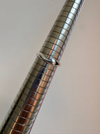 A polished silver metal ring displayed on a metallic measuring mandrel against a plain light gray background.
