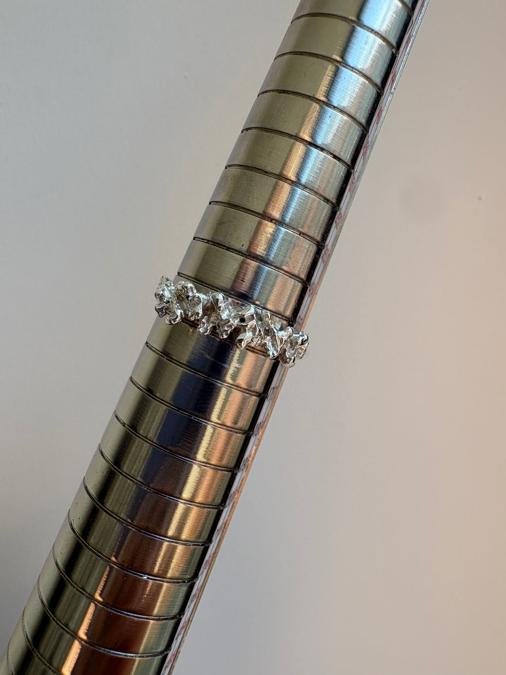 A silver ring with a row of clear triangular coral like crystals, displayed on a metallic cylindrical ring sizer against a plain light background.