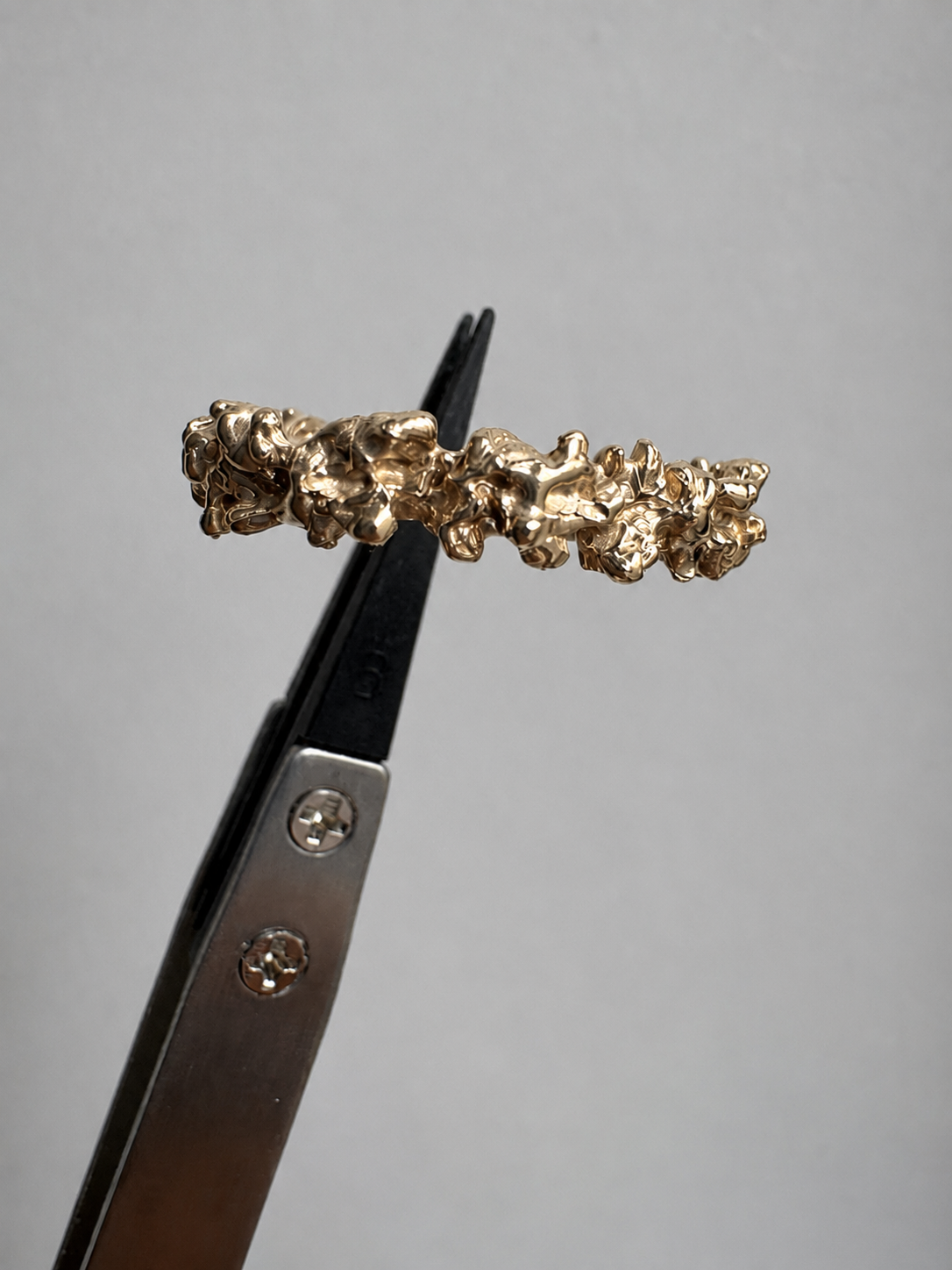14K Golden ring with dense textured surface all around held by pincet.