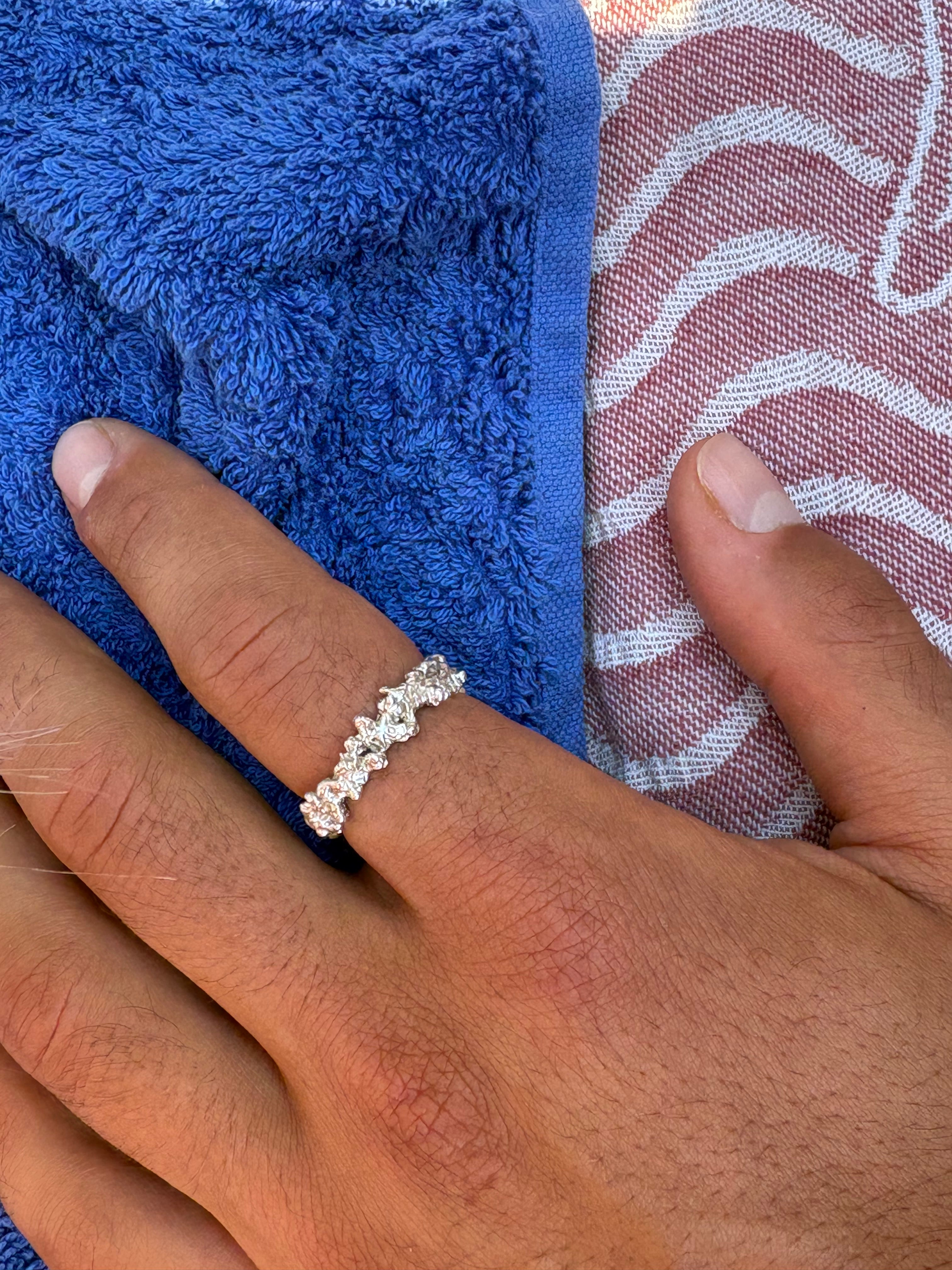 A close-up of a hand wearing a silver ring with small clear stones, resting on a blue towel over a patterned fabric.